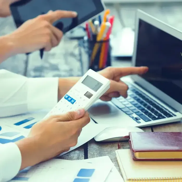 Hands using calculator beside laptop and tablet.